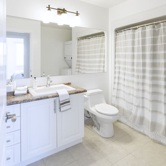a white bathroom with a toilet, sink, and shower curtain.