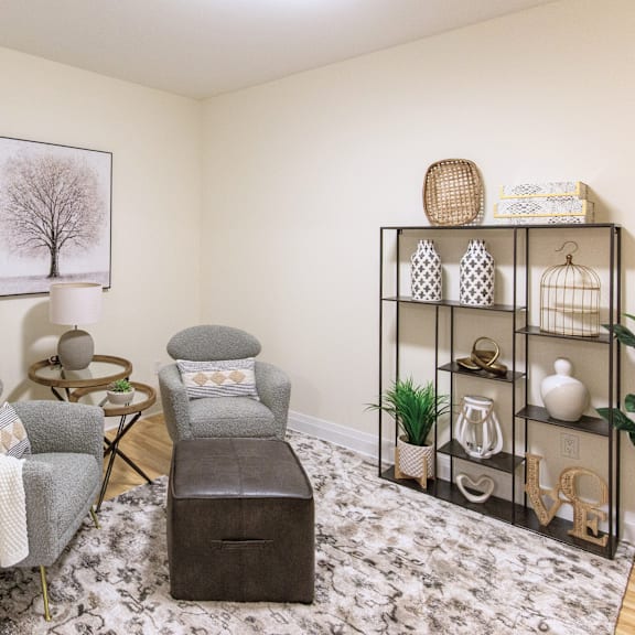 a living room with a grey chair, a small table, and a shelf with decorative items.