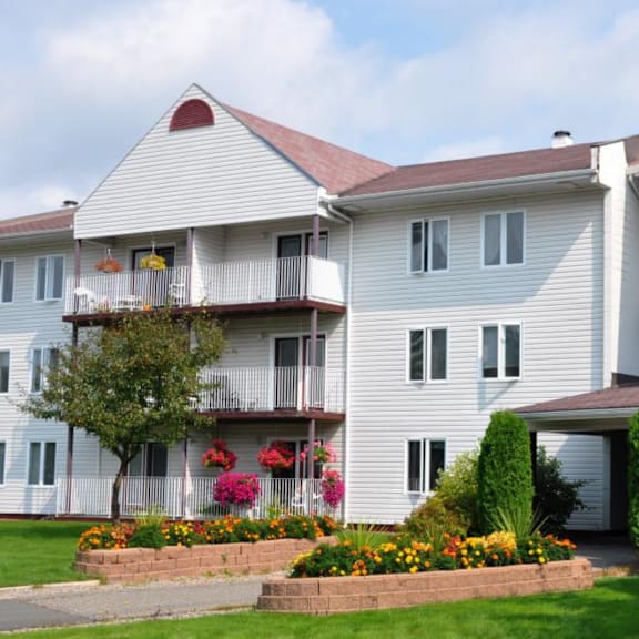 a white building with a red roof and a balcony with flowers.