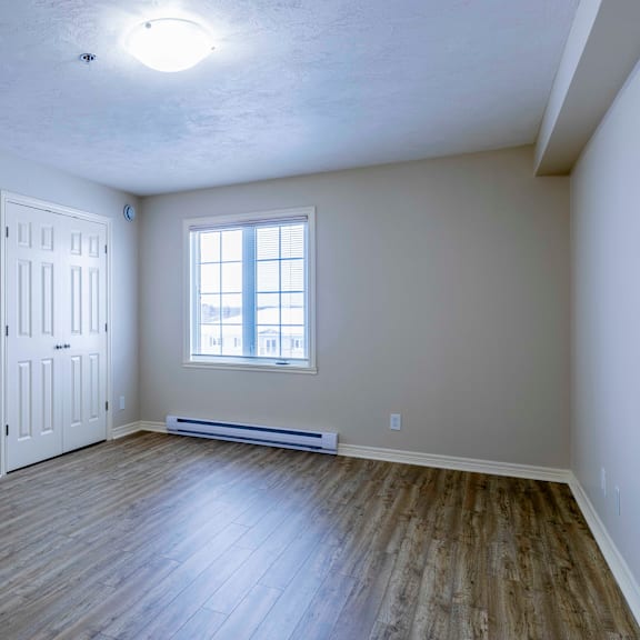 a room with a white door, a window, and a wooden floor.