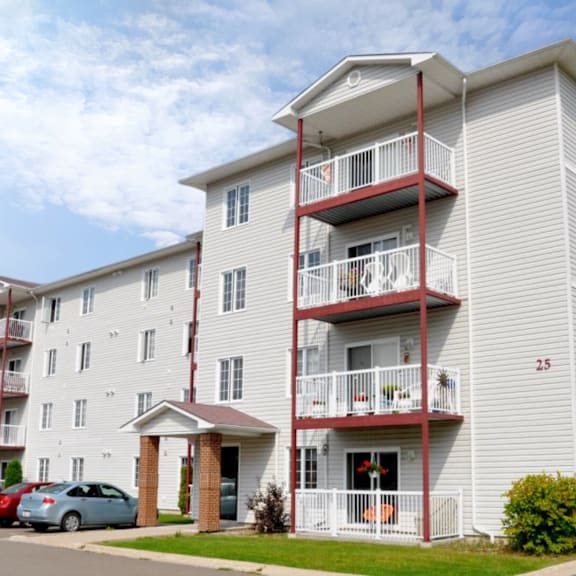a white apartment building with red balconies and a car parked in front.