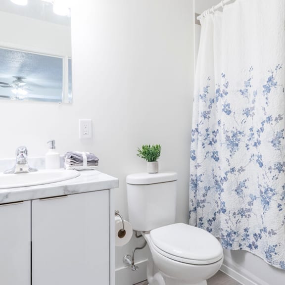 a white toilet with a white sink and a white cabinet with a blue and white shower curtain.