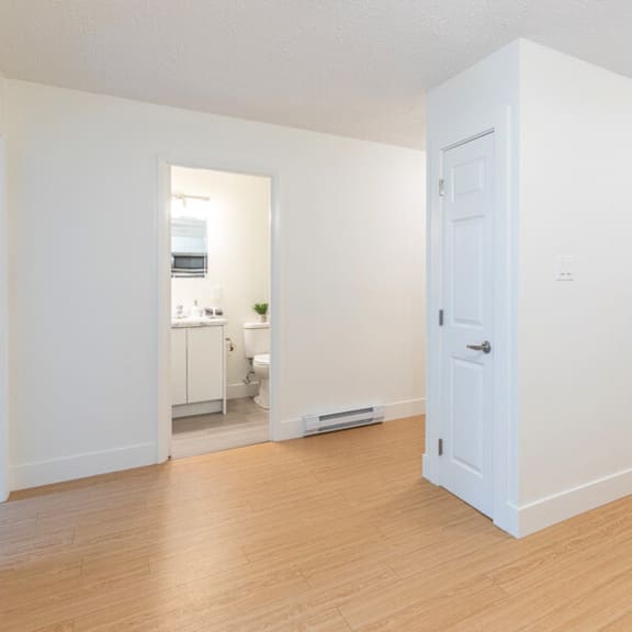 a white room with a door and a kitchen in the background.