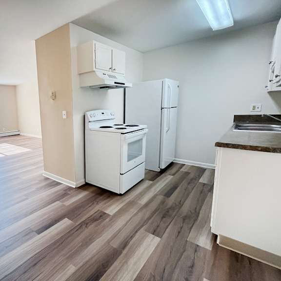 a kitchen with white appliances and wooden floors.