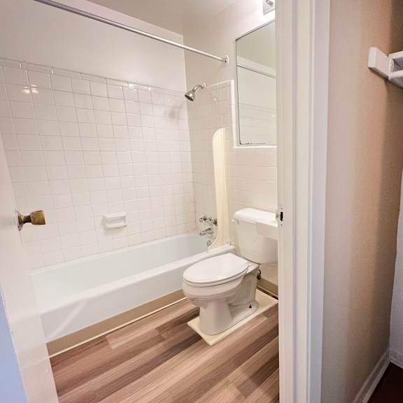 a white toilet in a small bathroom with a white bathtub and a white door.
