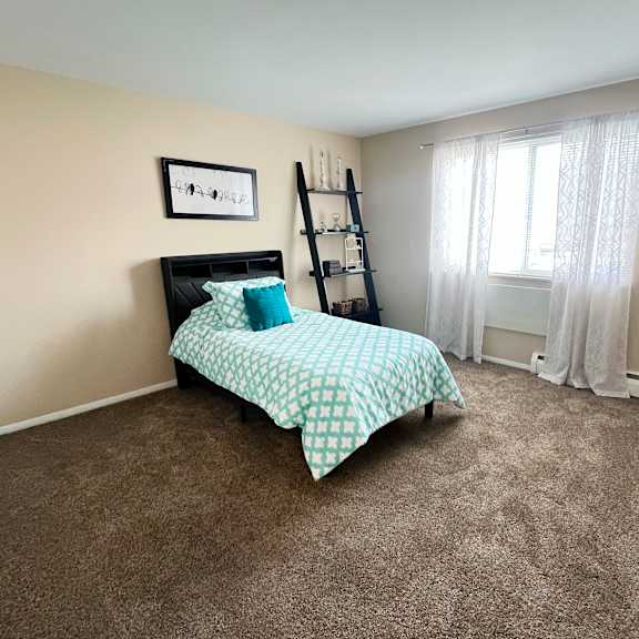 a bedroom with a bed, a window with curtains, and a shelf with items on it.