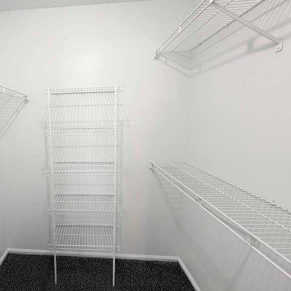 a walk-in closet with white shelving and a black carpeted floor.