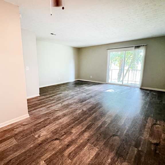 an empty living room with wood flooring and a sliding glass door at crown crossing apartments, amelia, ohio