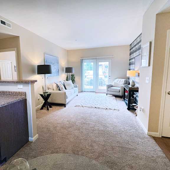 a living room with a couch, a chair, a rug, and a kitchen area with a sink and cabinets.