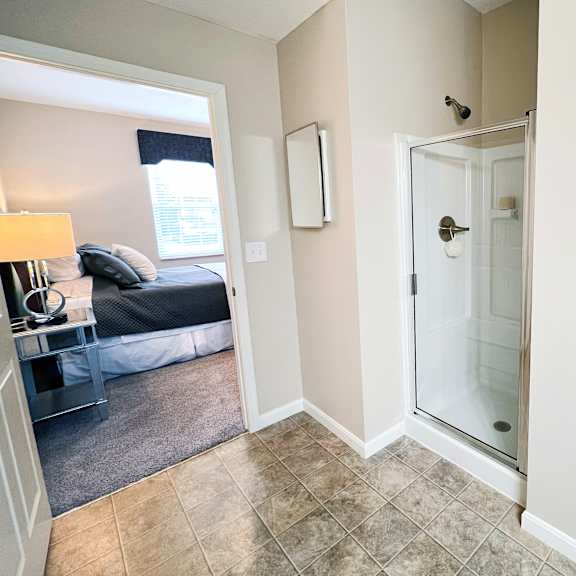 a bedroom with a bed, a chair, a mirror, and a shelf.