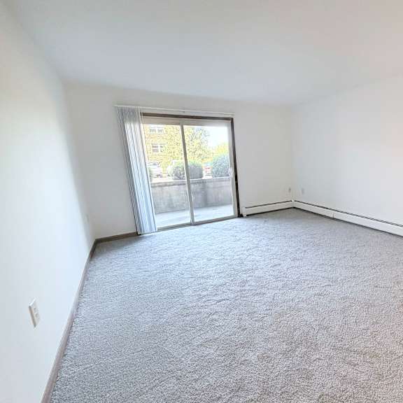 a spacious room with a carpeted floor and sliding glass doors leading to a balcony.