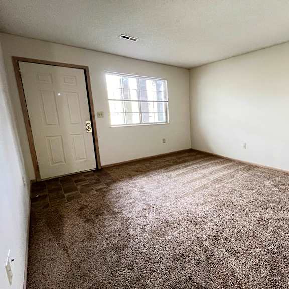 an empty living room with carpet and a door at eagle crest apartments, ohio