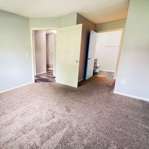 an empty living room with carpeting and a door to a bathroom at eagle crest apartments, galloway, 43119