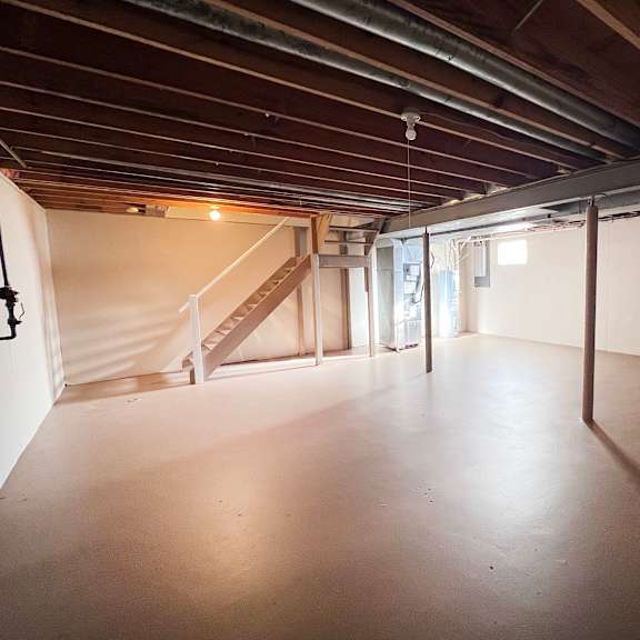 a spacious attic room with wooden beams and a staircase.