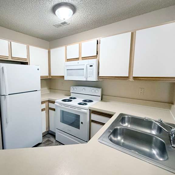 a kitchen with a white refrigerator, microwave, oven, and sink.