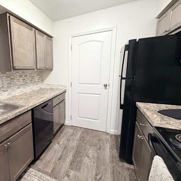 a kitchen with a black refrigerator and brown cabinets.