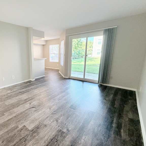 a spacious room with wood flooring and sliding glass doors leading to a green outdoor area.