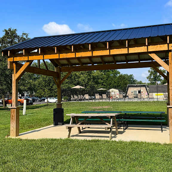 a wooden pavilion with a blue roof is situated in a grassy area.