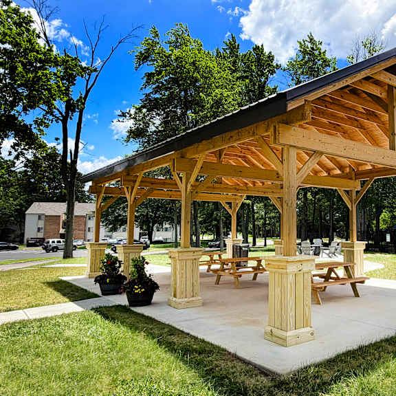 a wooden pavilion with picnic tables is surrounded by green grass.