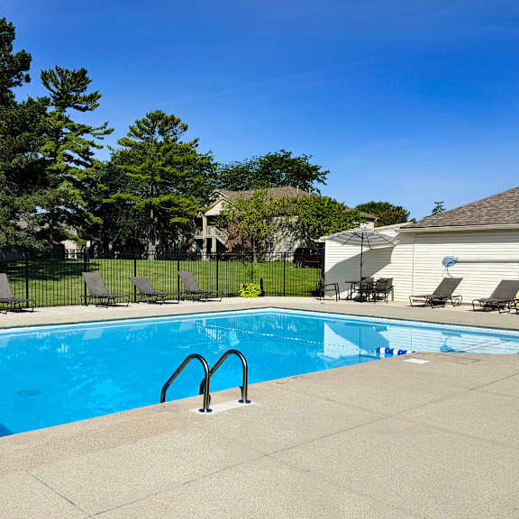 a swimming pool surrounded by a concrete patio and lounge chairs.