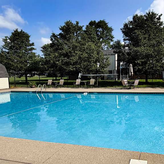 a large swimming pool surrounded by trees and a building in the background.