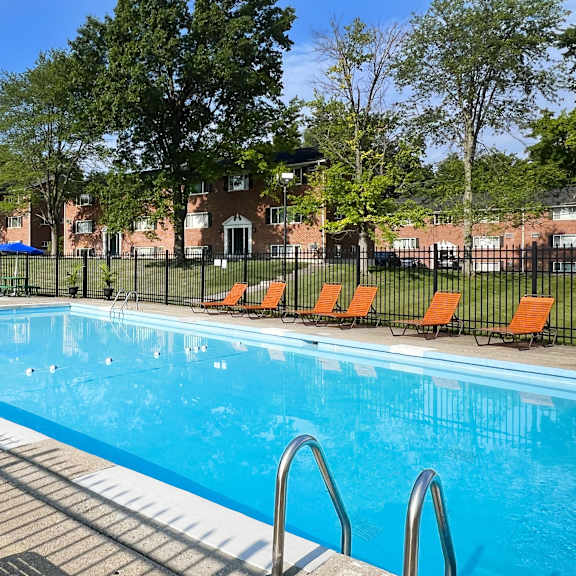 a swimming pool with orange chairs and a fence around it at sharondale woods apartments, cincinnati