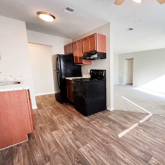 a kitchen with a black fridge and a wooden floor.
