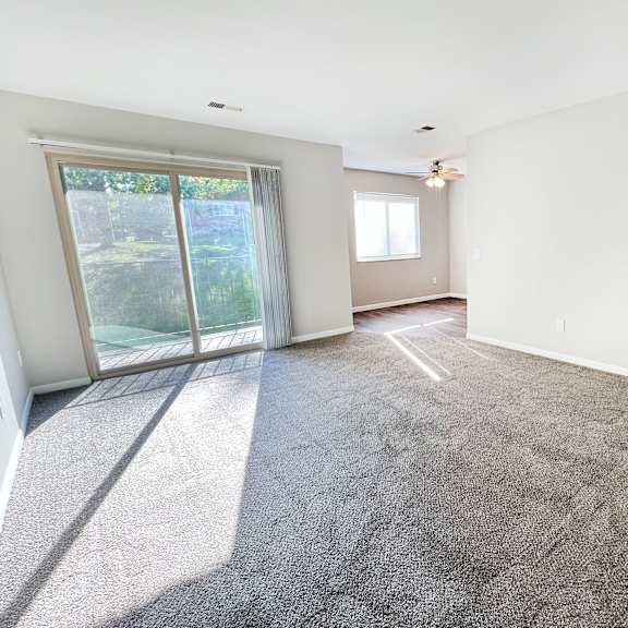 a spacious room with a carpeted floor and a sliding glass door leading to a backyard.