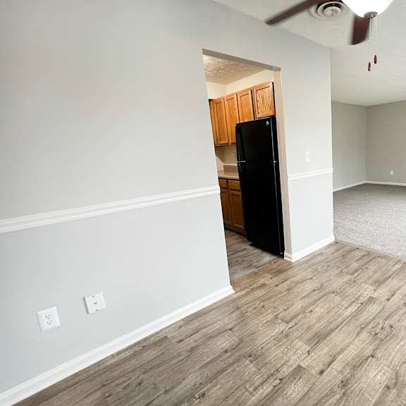 a room with a black fridge and wooden flooring.