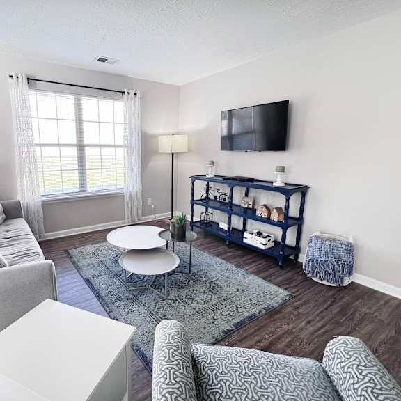 a living room with a grey couch, a white coffee table, a blue rug, and a tv mounted on the wall.