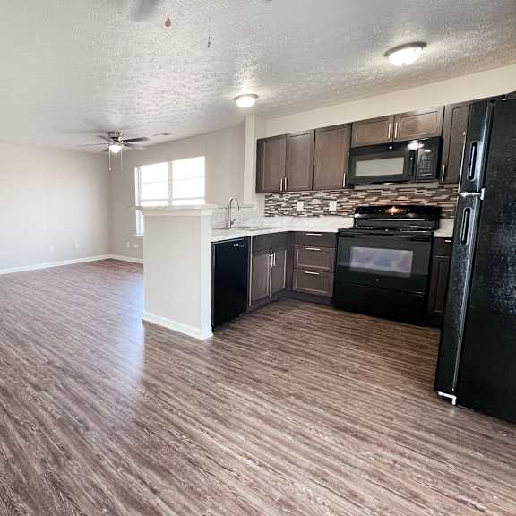 a kitchen with black appliances and wooden floors.