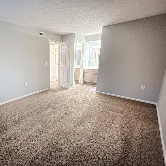 an empty living room with carpet and a door to a bathroom  at deercross apartments, cincinnati