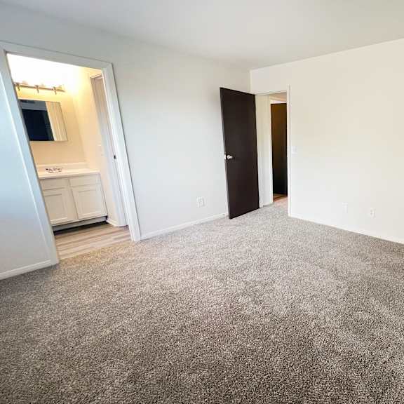 an empty living room with carpeting and a door to a bathroom at four worlds apartments, cincinnati, oh 45231