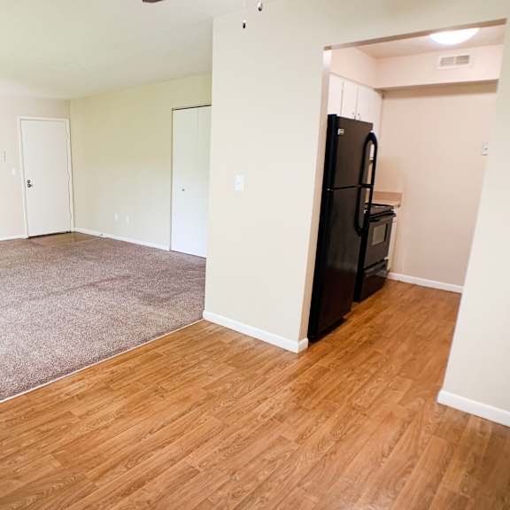 an empty living room with wood flooring and a black refrigerator  at hunter's creek apartments, cincinnati, oh