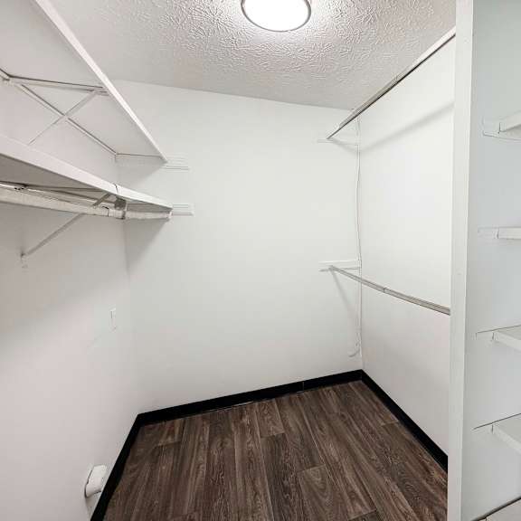 a walk-in closet with white shelves and a wooden floor.