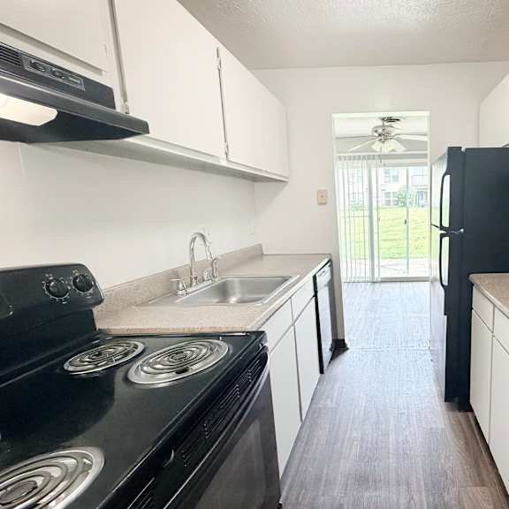 a black stove top oven sits in a kitchen with white cabinets and a black refrigerator.