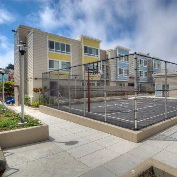 a basketball court is surrounded by a fence and a building with multiple windows.
