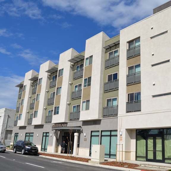 a modern building with a white facade and large windows is located on a street with cars parked in front.