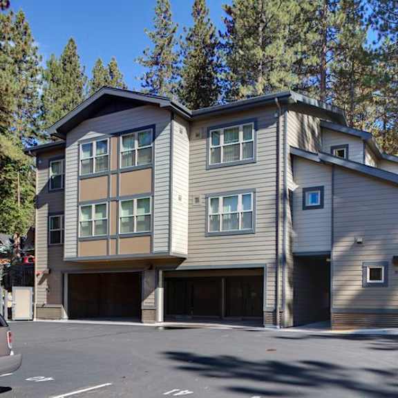 a two-story building with a garage is surrounded by trees.