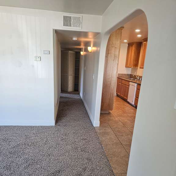 a hallway with a carpeted floor leads to a kitchen area.