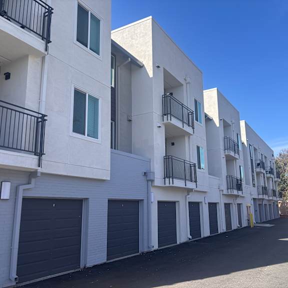a row of white apartment buildings with black railings and garage doors.