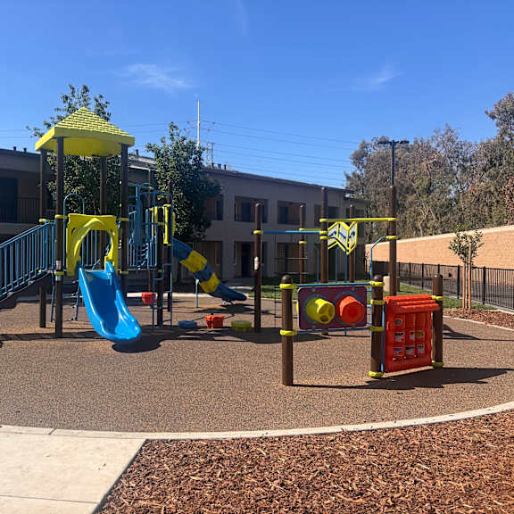 a playground with a yellow and blue slide, a red and yellow structure, and a green and yellow swing set.