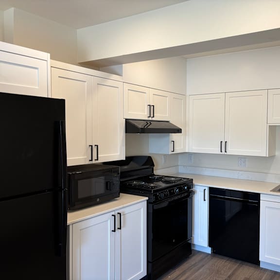 a black refrigerator is on the left in a kitchen with white cabinets.