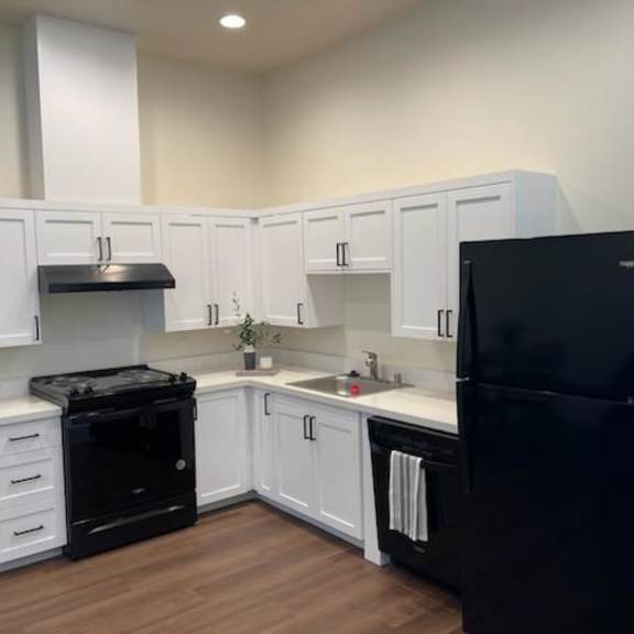 a black refrigerator sits in a kitchen with white cabinets.