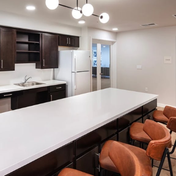 a modern kitchen with a long white island and brown chairs.