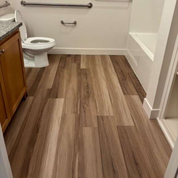 a white toilet sits in a bathroom with wood flooring.