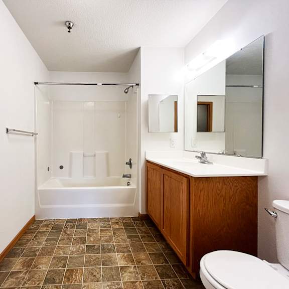 a bathroom with a white tub, brown tiles, and a white toilet.