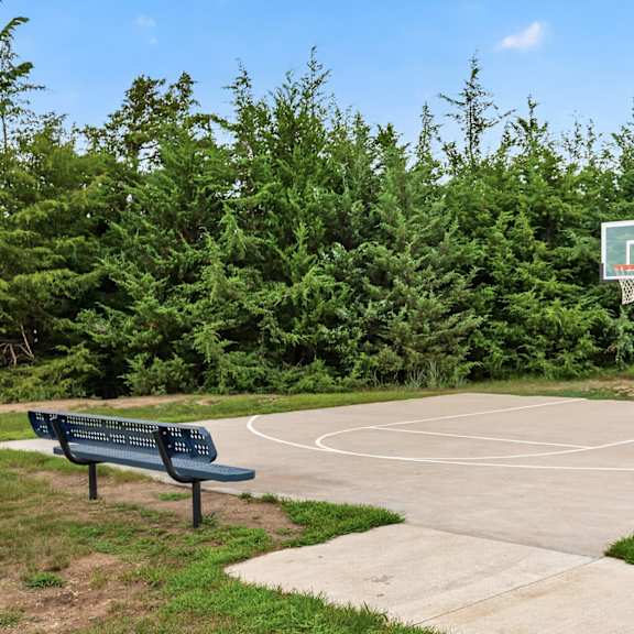 a basketball court surrounded by green trees and a bench.