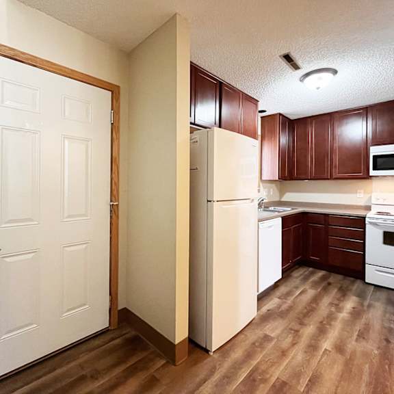a white door is open to a kitchen with brown cabinets.