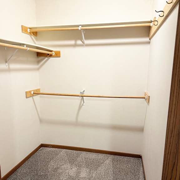 a walk in closet with a grey carpet and two shelves.